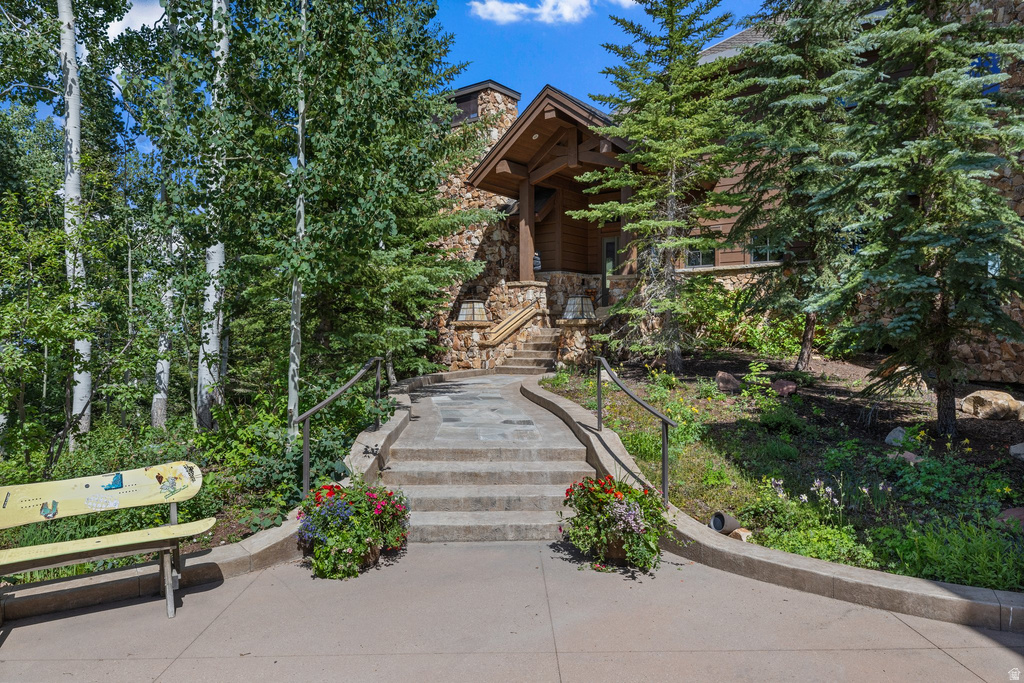 Stone facade home with a covered entry featuring exposed timber beams, a stone pathway, and mature trees