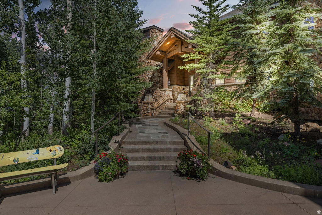 Stone and wood-sided exterior featuring a covered entry, stone steps with handrails, and surrounding mature trees