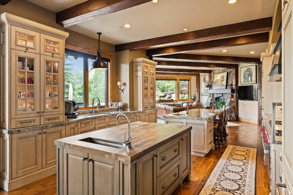 Gourmet kitchen with two islands, light-toned cabinetry with glass-front uppers, wood-finish flooring, and exposed ceiling beams