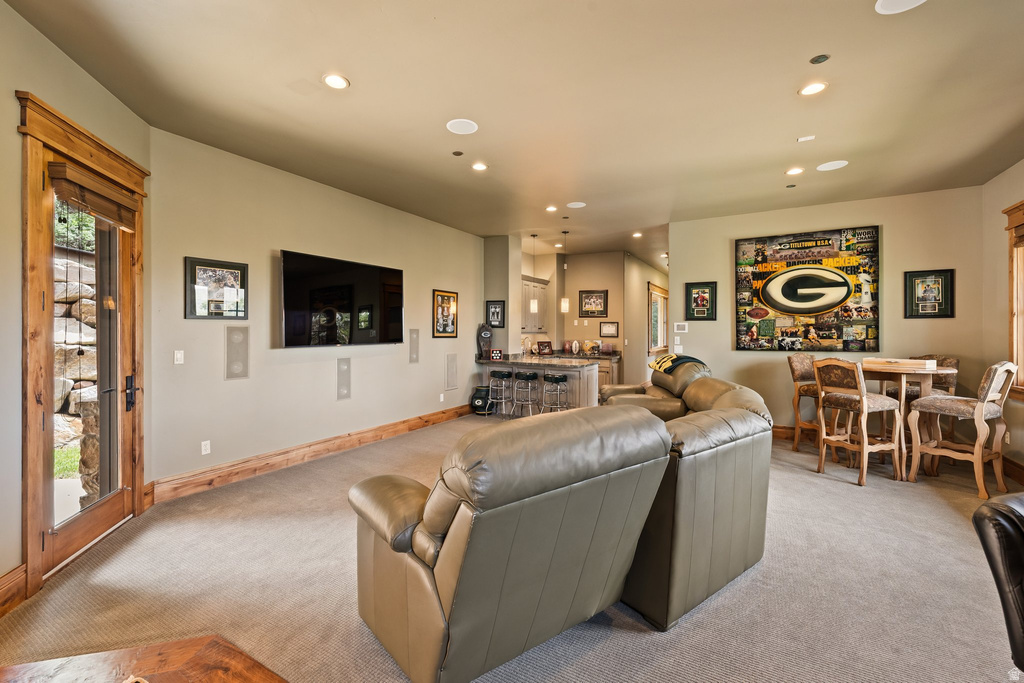 Spacious recreation area featuring recessed lighting, carpet flooring, a built-in media wall, and a wet bar with pendant lighting and bar seating