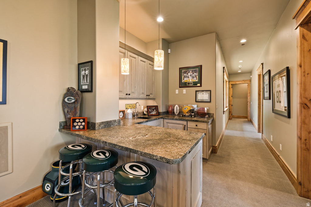 Built-in wet bar featuring a stone countertop, light wood-finish cabinetry, and pendant lighting