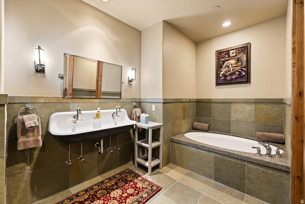 Bathroom featuring a wall-mounted trough sink with two faucets, a built-in soaking tub with a stone-finish deck, slate-style wall tiling, and coordinating floor tiles