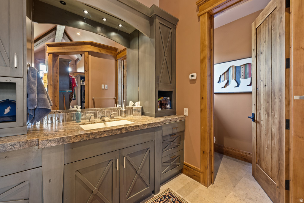 Vanity with a stone countertop, integrated sink, and gray cabinetry featuring cross-brace detailing