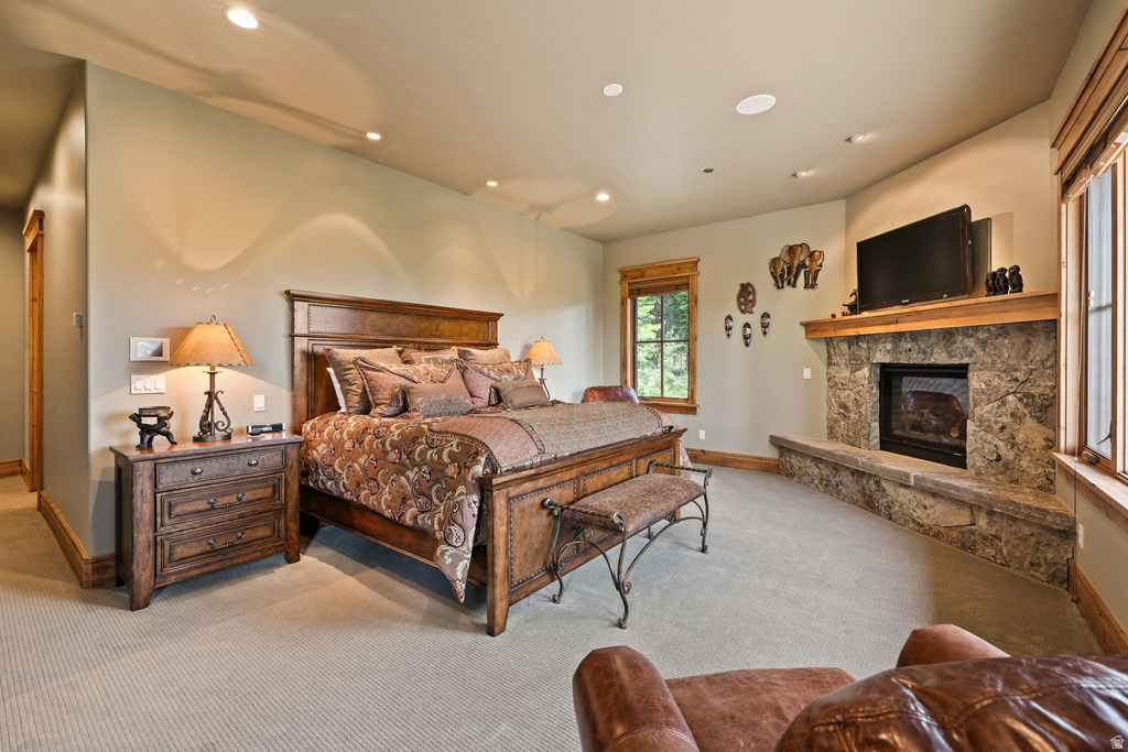 Carpeted room featuring a stone fireplace with a wood mantle, recessed lighting, and multiple windows with wood trim