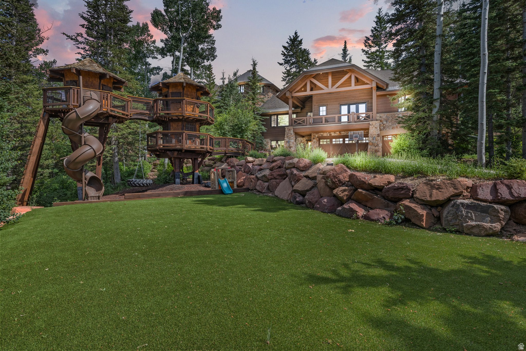 Expansive synthetic turf lawn with a multi-level wooden play structure featuring slides and elevated platforms