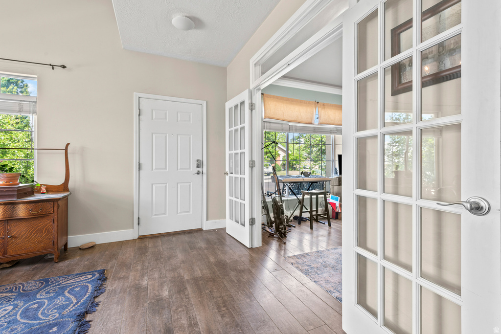 Interior entry area featuring wood-finish flooring, a white paneled door, and white French doors opening into an additional room