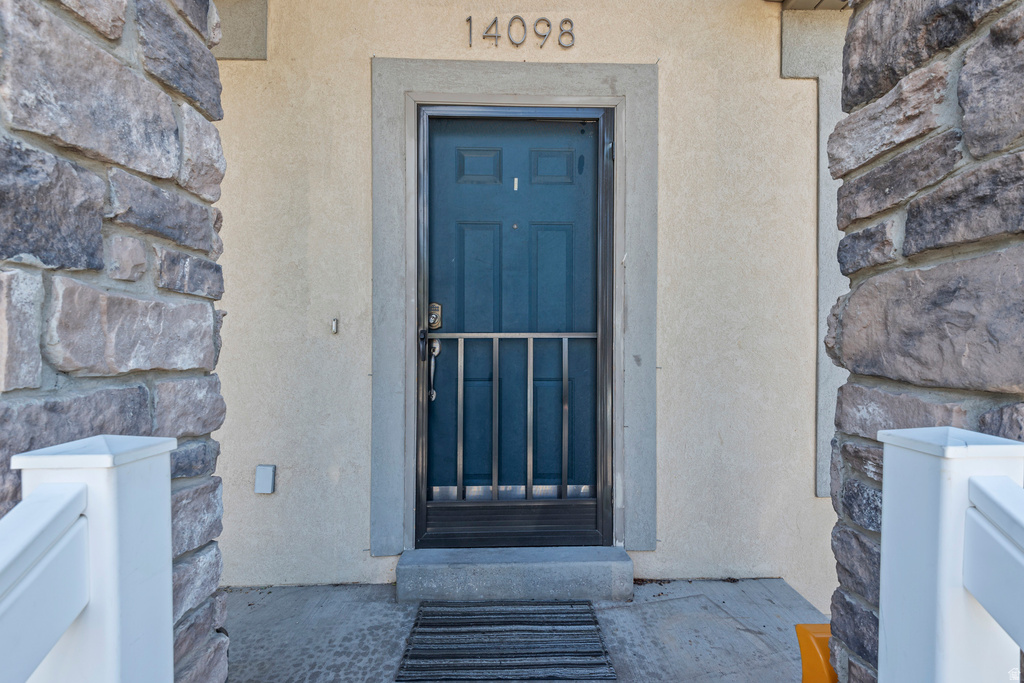Entryway featuring a dark blue door with security screen, stone facade pillars, and a stucco exterior finish