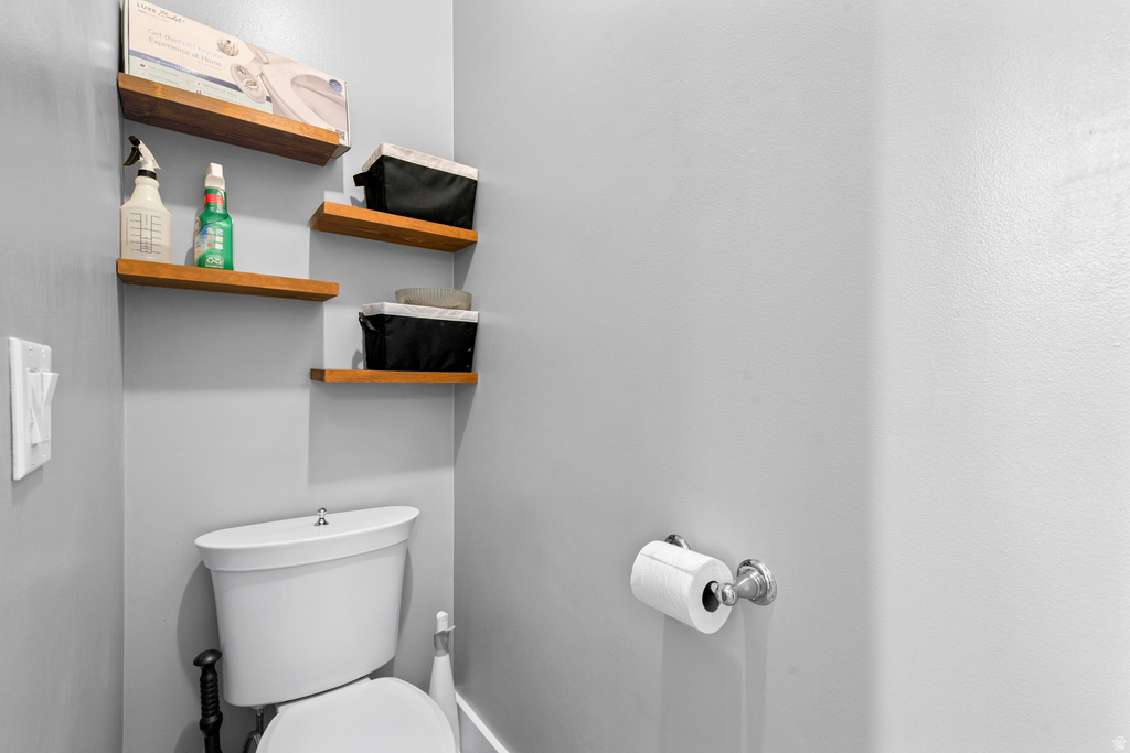Recessed toilet alcove featuring three floating wood shelves, a built-in toilet, and a chrome toilet paper holder