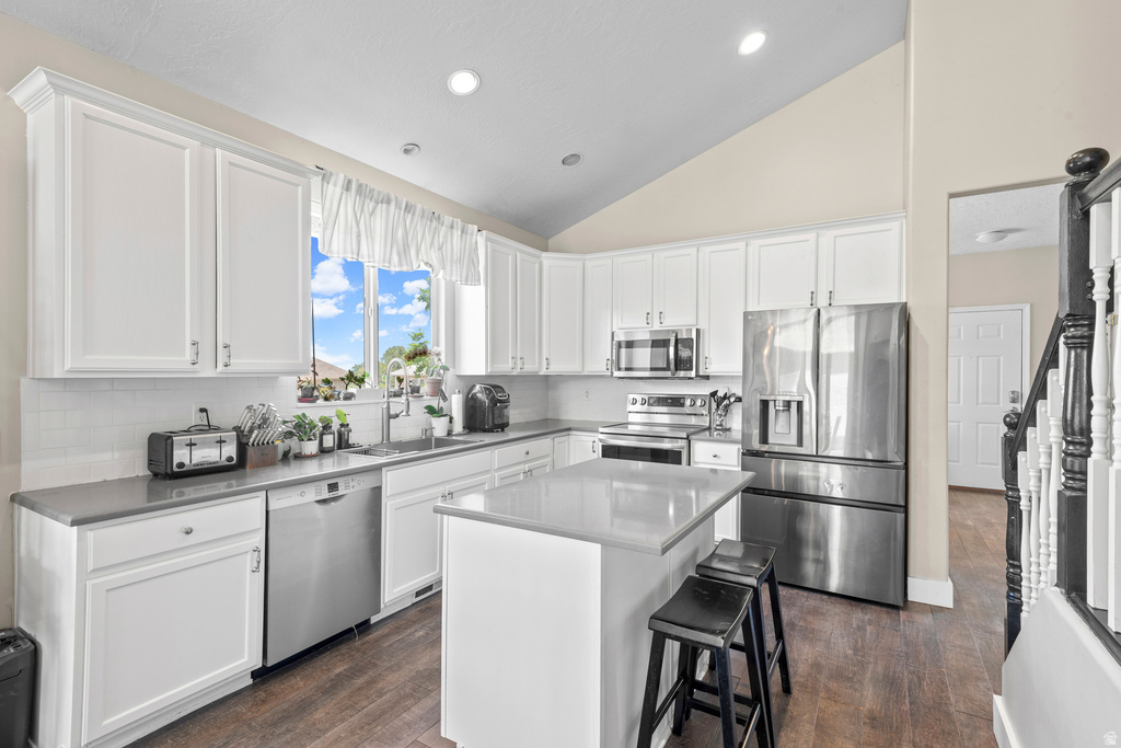 Bright kitchen featuring white cabinetry, stainless steel appliances, a center island with countertop seating, and wood-finish flooring