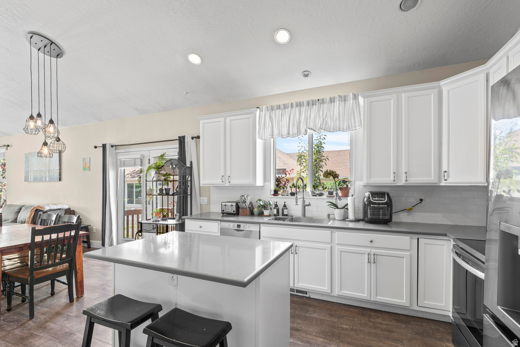 Kitchen featuring a central island with a solid surface countertop, white shaker-style cabinetry, a stainless steel sink with a gooseneck faucet, light grey subway tile backsplash, and wood-finish flooring