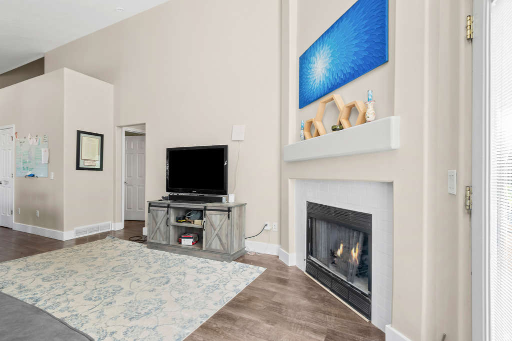 Living area featuring vaulted ceilings, wood-finish flooring, a corner fireplace with white tile surround, and a white mantel