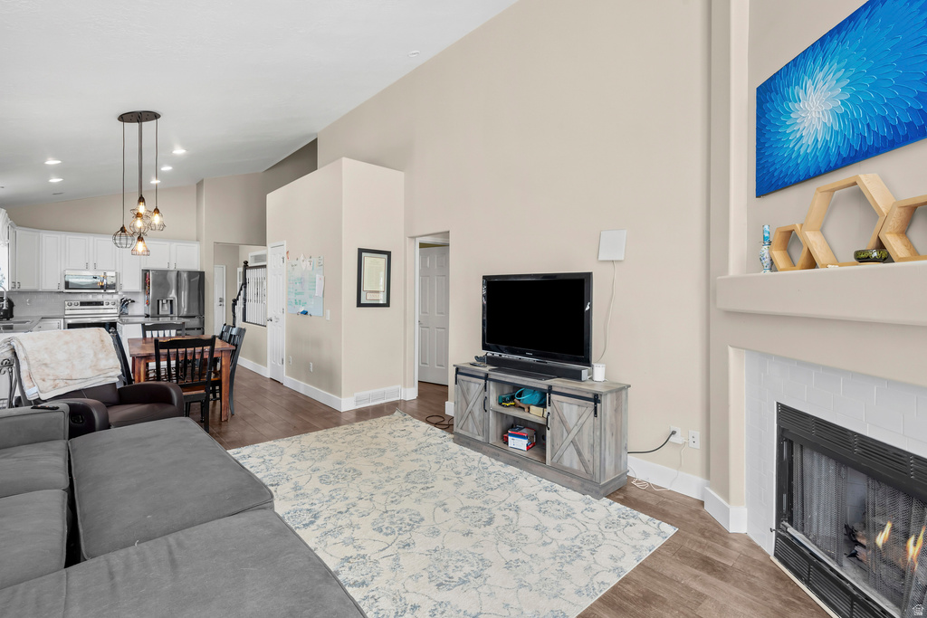 Expansive living area featuring vaulted ceilings, wood-finish flooring, and a fireplace with a white tile surround
