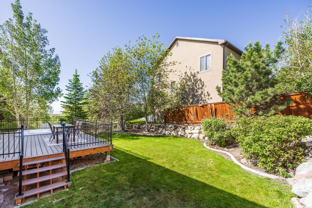 Expansive backyard featuring a multi-level deck with black metal railings, a manicured lawn, and mature trees