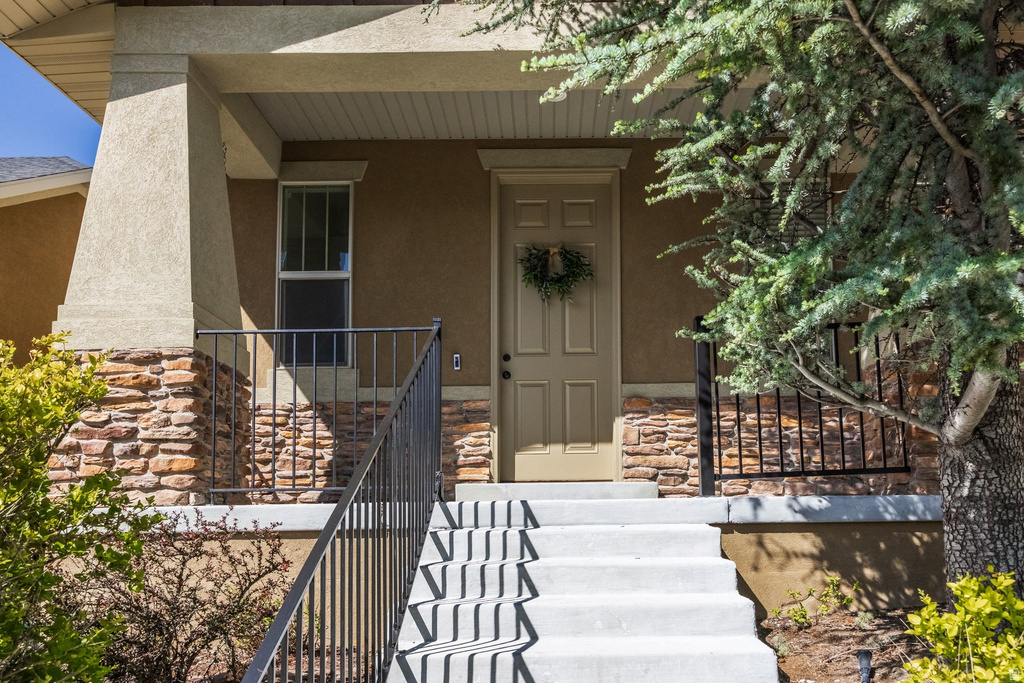 Front entrance featuring a covered porch, stone veneer accents, concrete steps with wrought iron railings, and a panel door