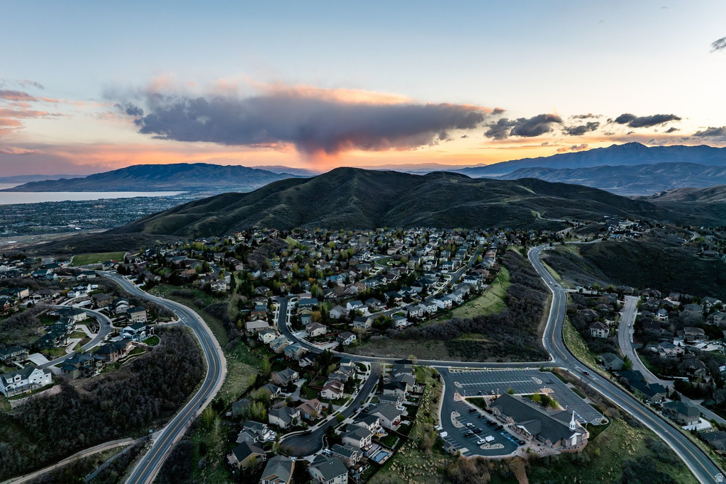Hillside community featuring residential properties, winding roads, a prominent commercial structure, and distant water and mountain backdrops