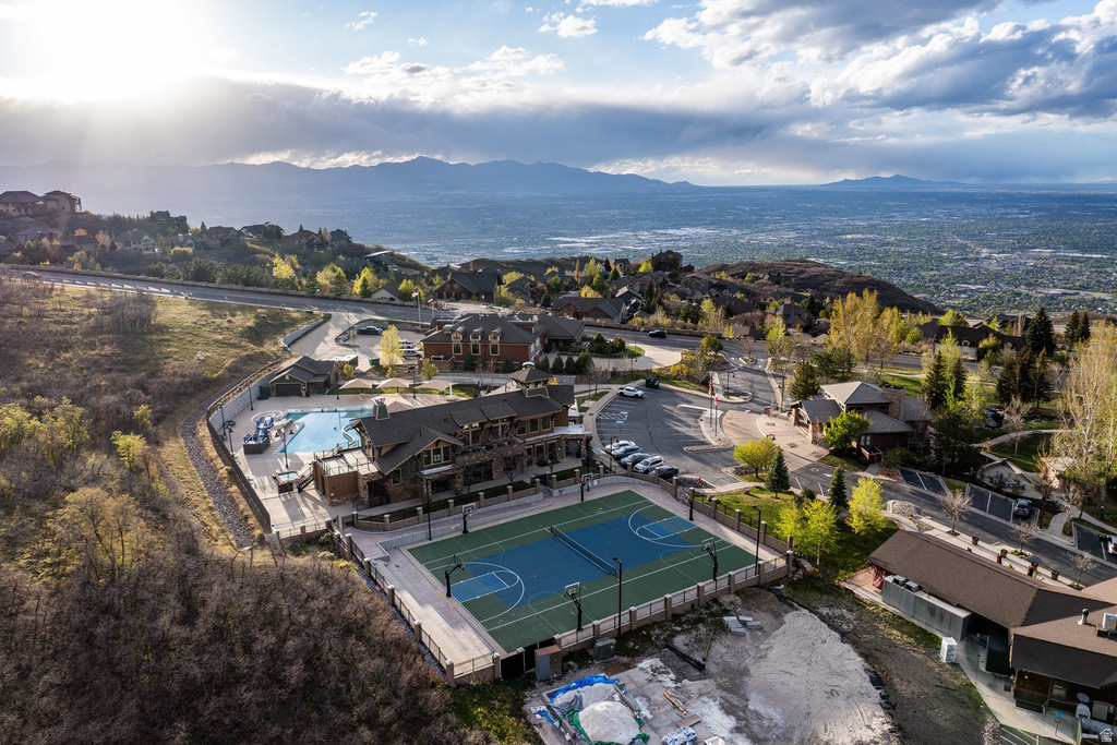 Elevated property featuring a multi-sport court with basketball markings, a swimming pool, and a clubhouse building with stone and wood siding