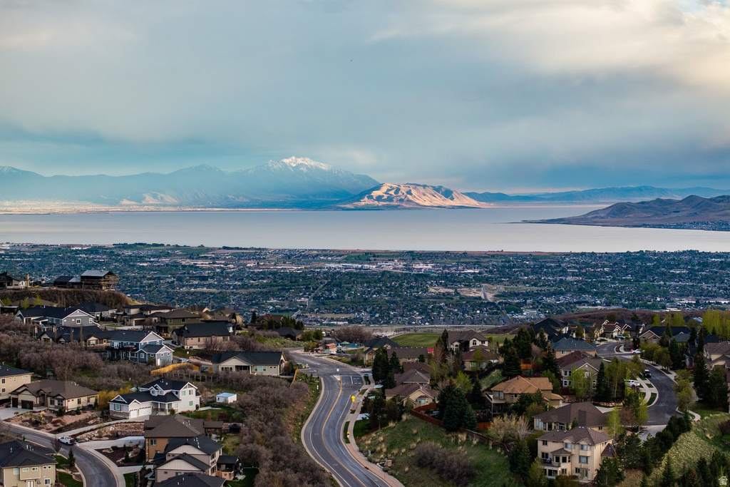 Neighborhood featuring a winding street, established homes, abundant mature trees, distant water body, and a mountainous backdrop