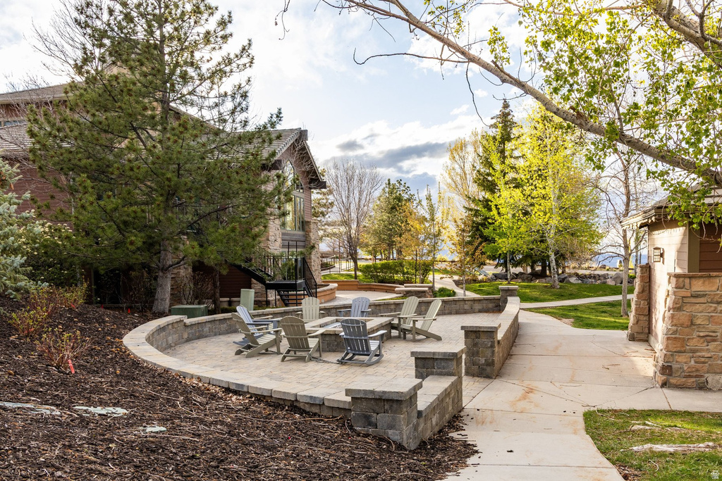 Paved patio with an integrated fire pit, surrounded by a stone retaining wall and mature trees