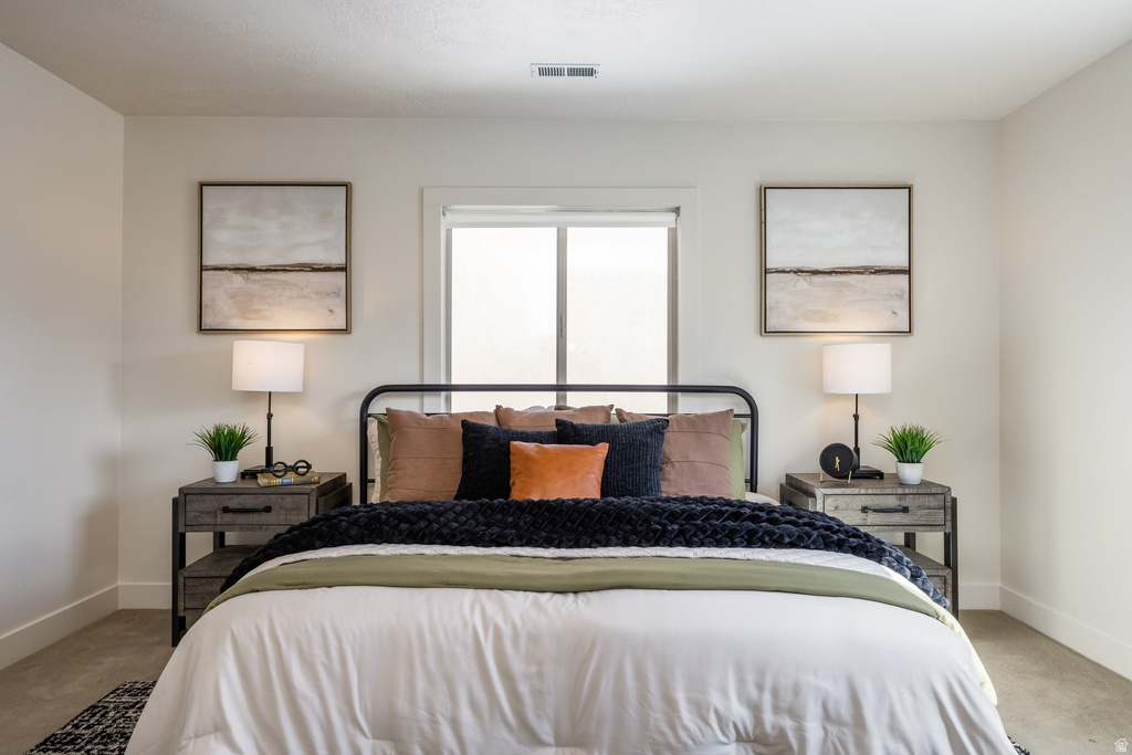 Bright bedroom with a centrally placed window, light wall paint, and carpeted flooring