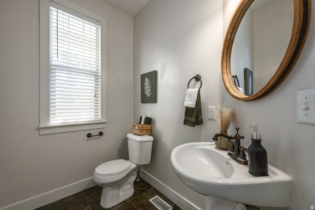 Pedestal sink with dark bronze faucet, wall-mounted mirror with a wood-finish frame, and stone-finish tile flooring