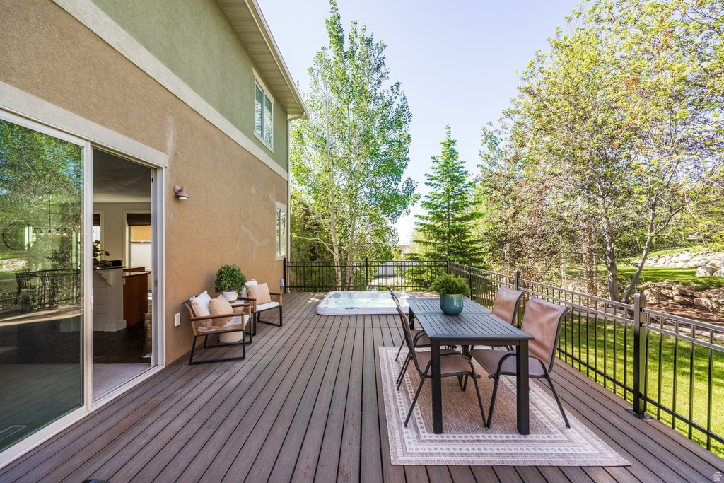 Expansive wood-finish deck with a built-in hot tub, black metal railing, and direct access to interior spaces via sliding glass doors