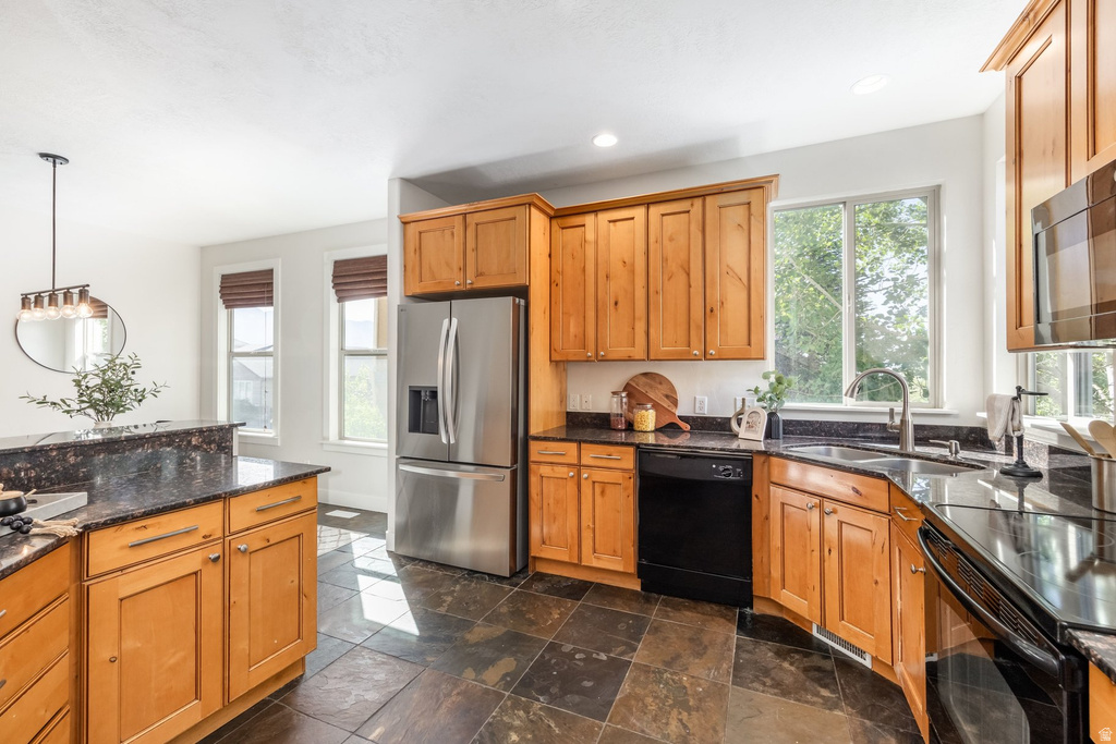 Kitchen featuring wood cabinetry, dark stone countertops, stainless steel refrigerator, black dishwasher, and stone tile flooring