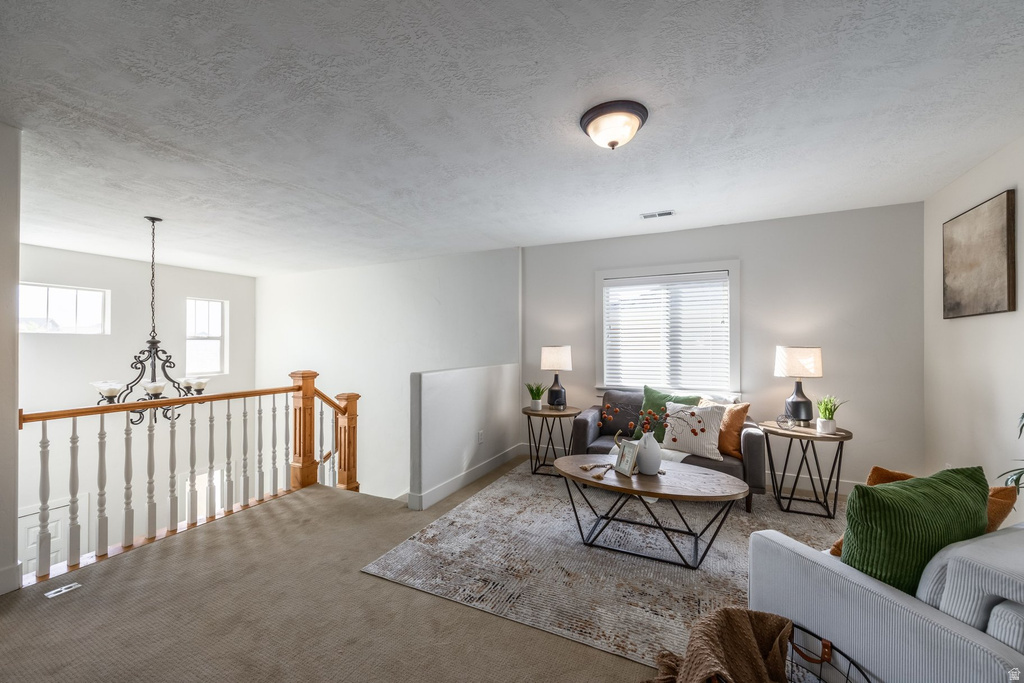 Carpeted upstairs landing featuring a staircase with wood newel posts and banister, white balusters, and a black wrought iron chandelier