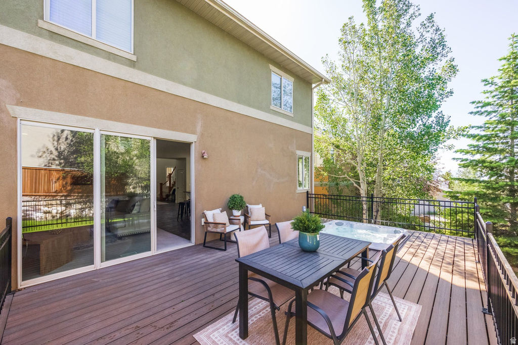 Expansive composite deck featuring a built-in hot tub, black metal railings, and direct access to interior spaces through a multi-panel sliding glass door