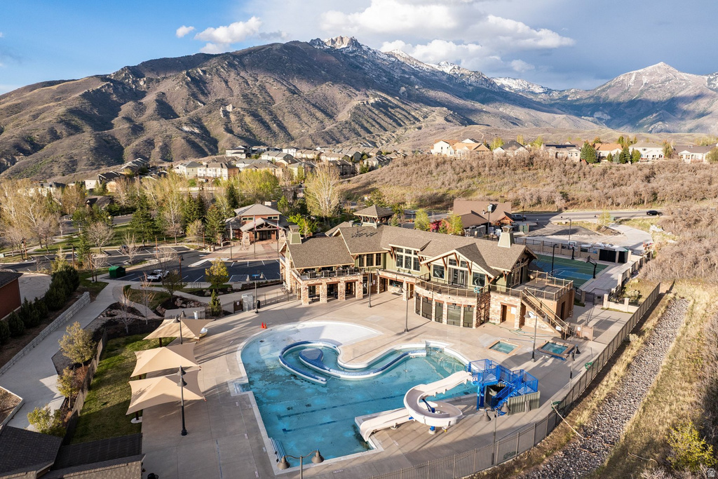 Mountain-framed community hub featuring an outdoor pool with water slide, multiple hot tubs, and shaded patio areas