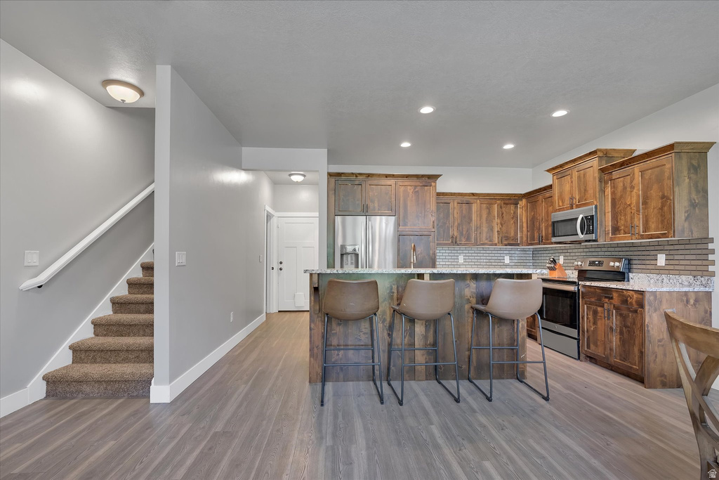 Open-concept kitchen featuring wood-finish cabinetry, stainless steel appliances, a multi-tonal backsplash, and granite-style countertops