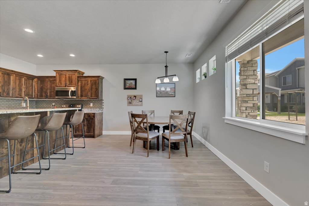 Open-concept kitchen and dining area featuring wood-finish flooring, recessed lighting, and a window with a stone accent column