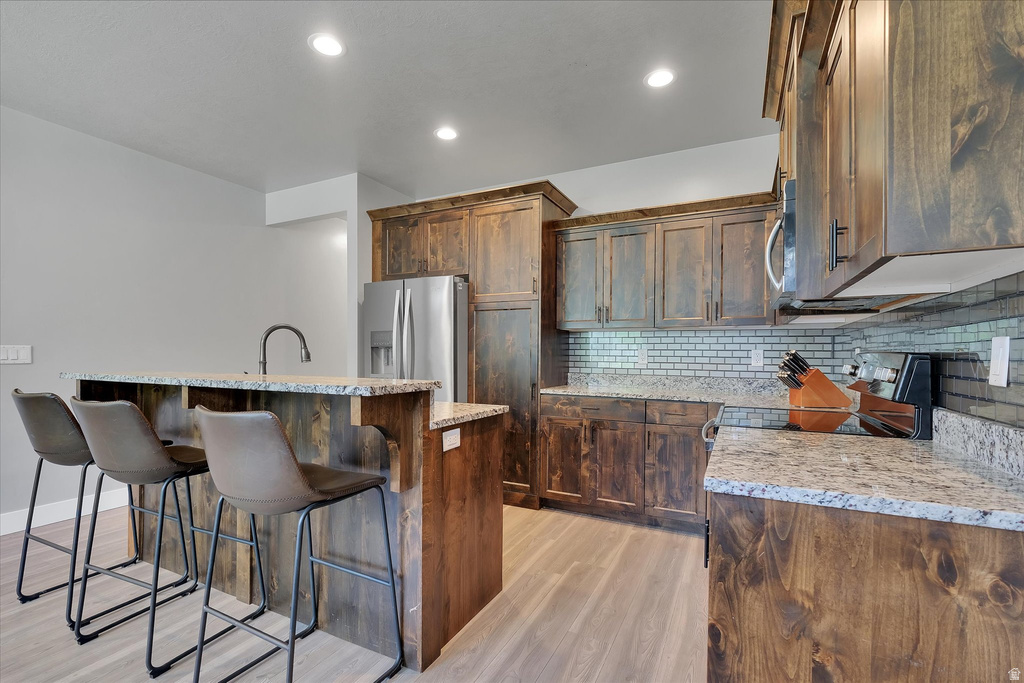 Kitchen featuring wood-finish cabinetry, light-toned wood-finish flooring, granite countertops, and a subway tile backsplash