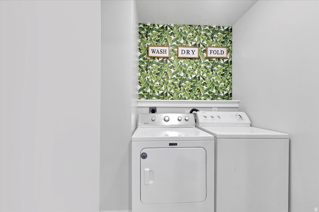 Dedicated laundry area featuring white appliances, a white shelf, and decorative leaf-patterned wallpaper