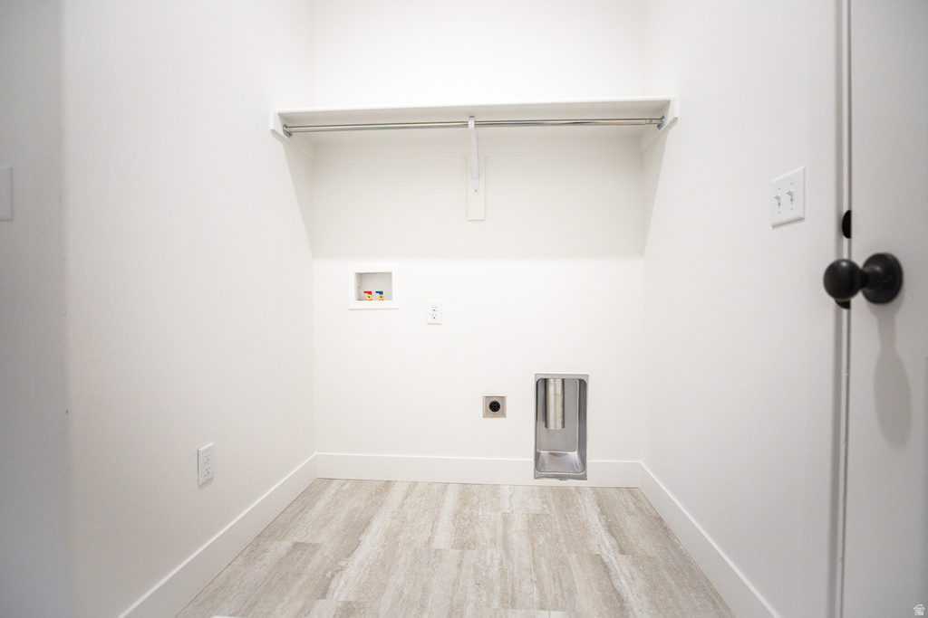 Dedicated utility space featuring light wood-finish flooring, white walls, and a built-in shelf with a chrome hanging rod