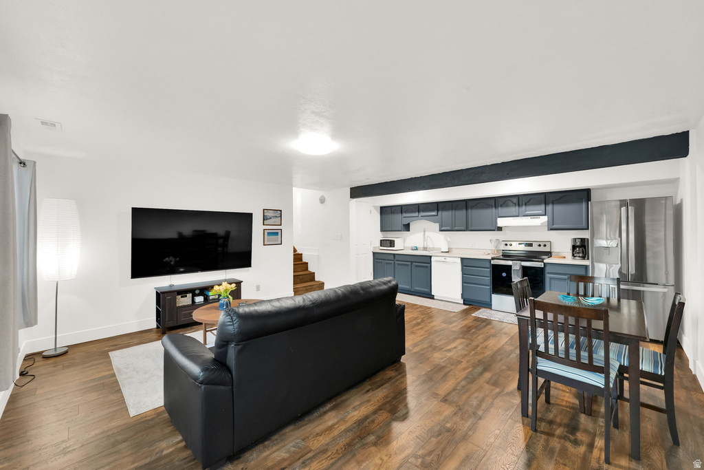 Open-concept living space featuring wood-finish flooring, a kitchen with blue cabinetry and stainless steel appliances, and a dining area
