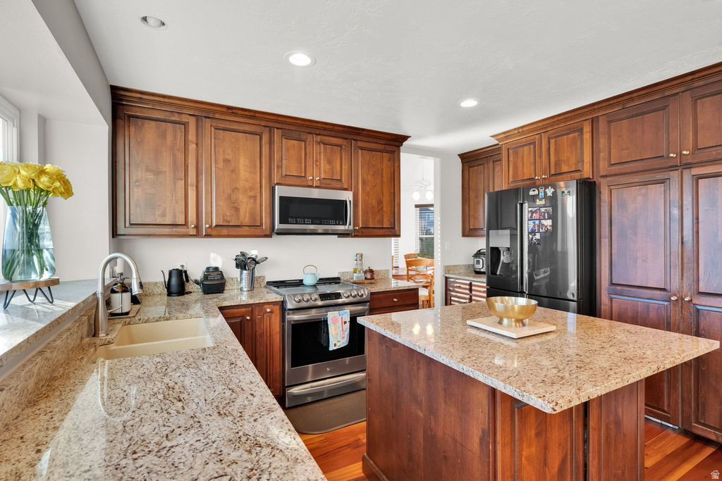 Kitchen featuring wood cabinetry, light-toned countertops, a stainless steel range with overhead microwave, a dark-finish refrigerator, and a central island