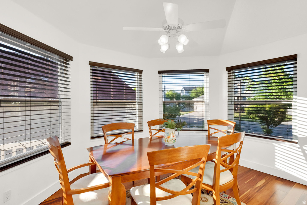 Dining area featuring a prominent bay window with multiple windows, wood-finish flooring, a vaulted ceiling, and a ceiling fan with integrated lighting