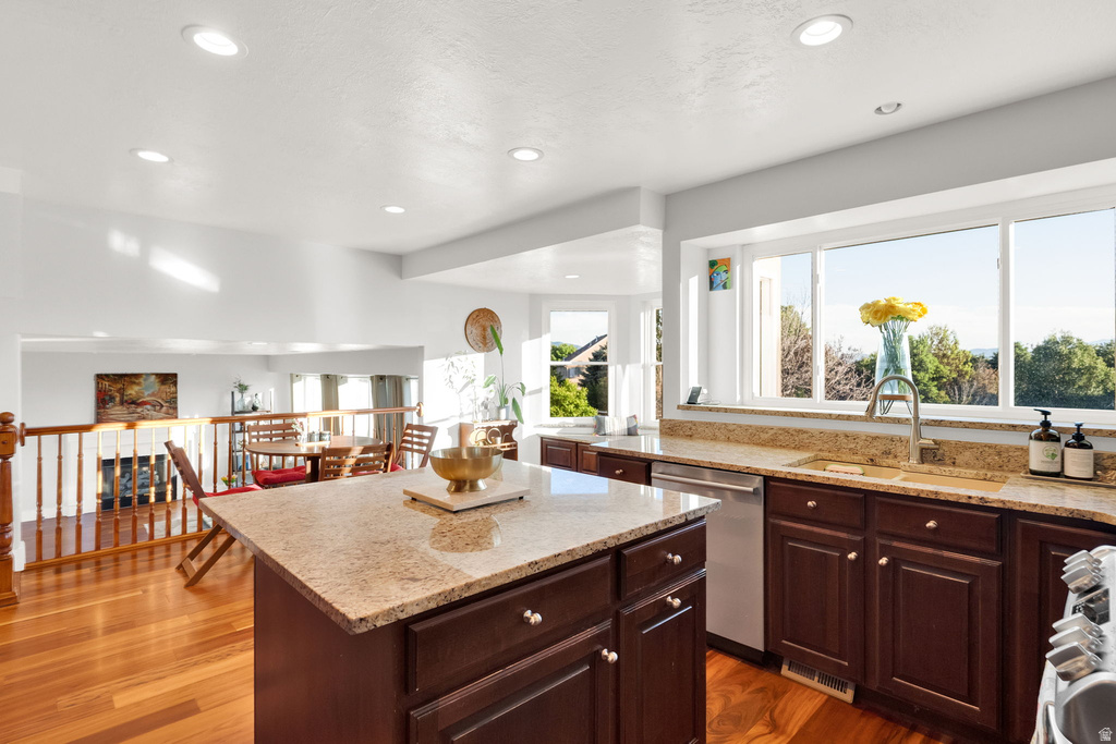 Kitchen featuring a central island with a granite countertop, recessed lighting, wood-finish flooring, dark wood cabinetry, and a stainless steel dishwasher