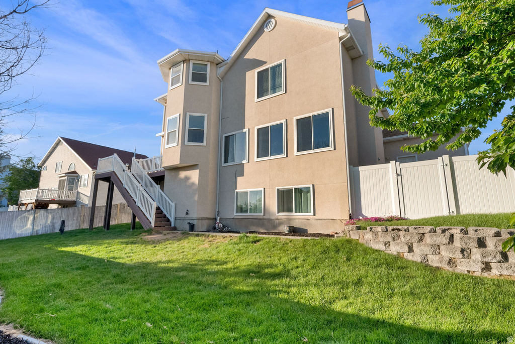 Stucco exterior with multiple windows, a multi-level deck featuring white railings, a terraced retaining wall, and a white privacy fence