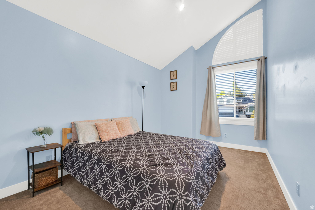 Vaulted ceiling bedroom featuring a large arched window with horizontal blinds, light blue painted walls, and brown carpet flooring