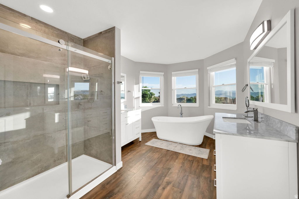 Modern bathroom featuring a freestanding soaking tub, separate glass-enclosed shower, wood-finish flooring, dual vanity with undermount sinks, and multiple windows