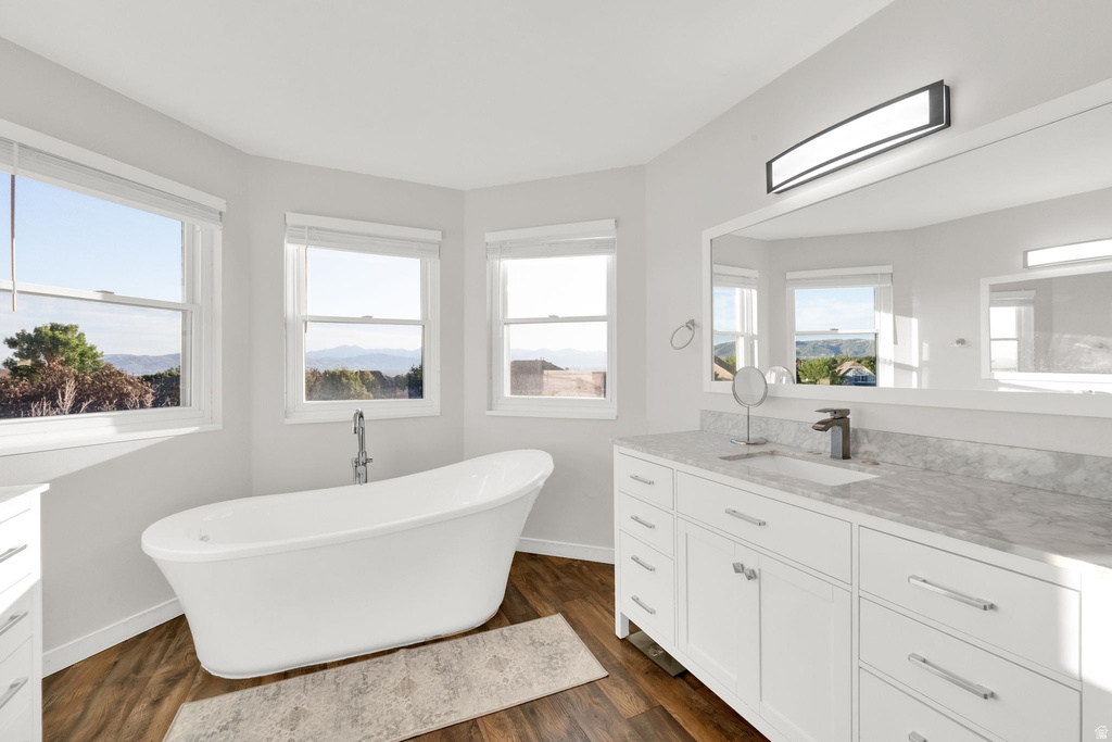 Modern bathroom featuring a freestanding soaking tub, wood-finish flooring, white vanity with stone countertop, and an expansive mirror