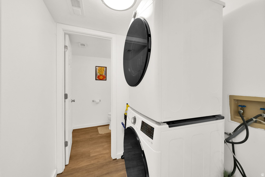 Dedicated laundry area featuring a stacked washer and dryer, wood-finish flooring, and a round overhead light fixture