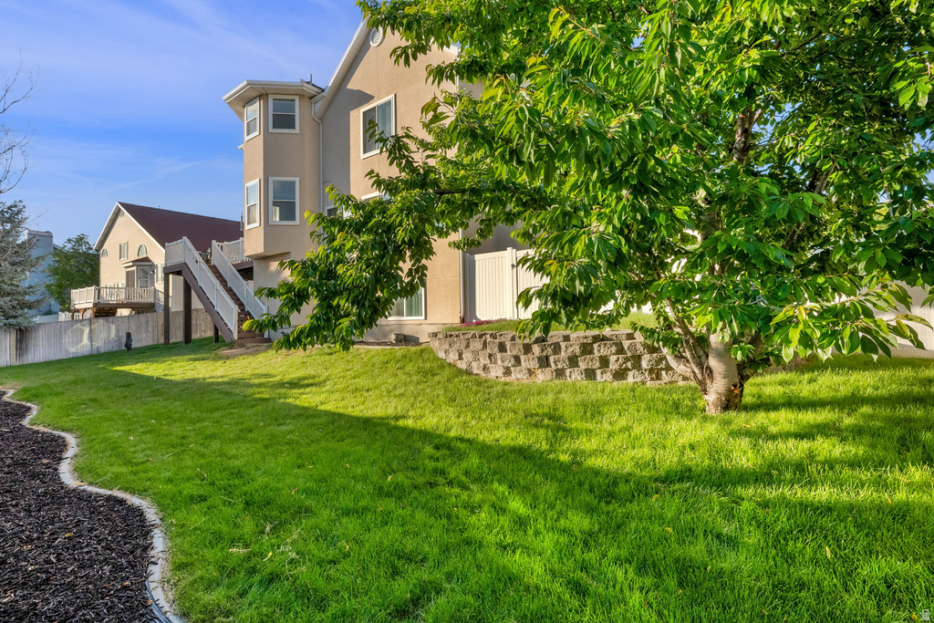 Expansive rear yard featuring green lawn, a retaining wall, mature tree, and a curved landscaped border