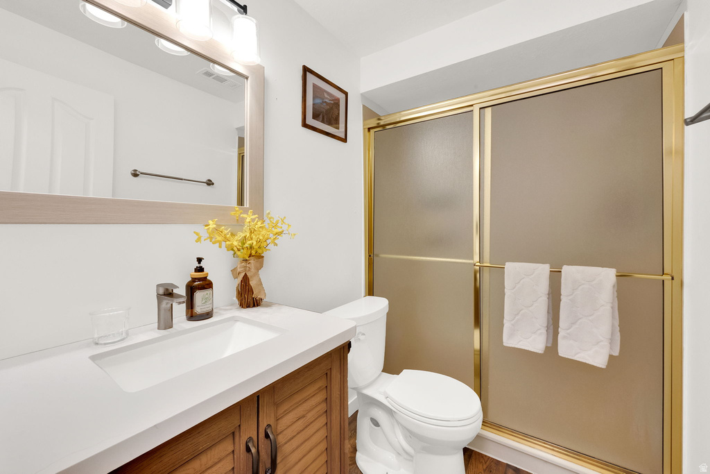 Bathroom featuring a gold-framed shower enclosure with frosted glass, a white toilet, and wood-finish vanity with a white countertop and integrated sink