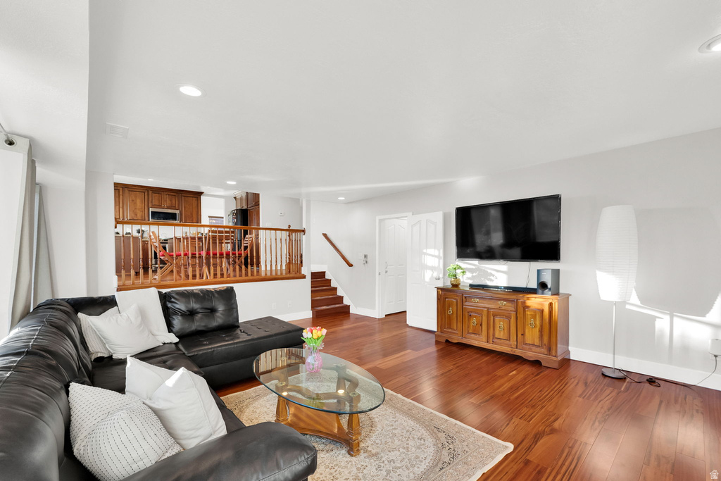 Open-concept living space featuring wood-finish flooring, recessed lighting, and a partial wall with wood railing overlooking a kitchen area with wood cabinetry