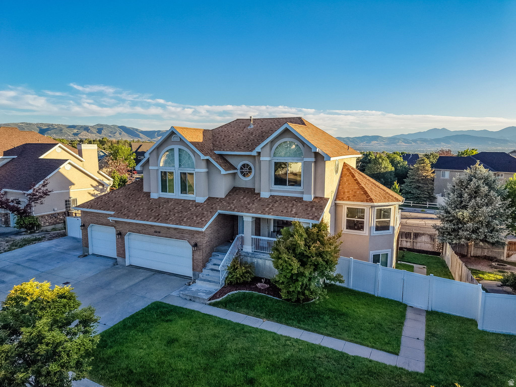 Two-story residence featuring a tan stucco and brick exterior, a multi-car driveway, arched windows, a front entry staircase, and fenced yard space