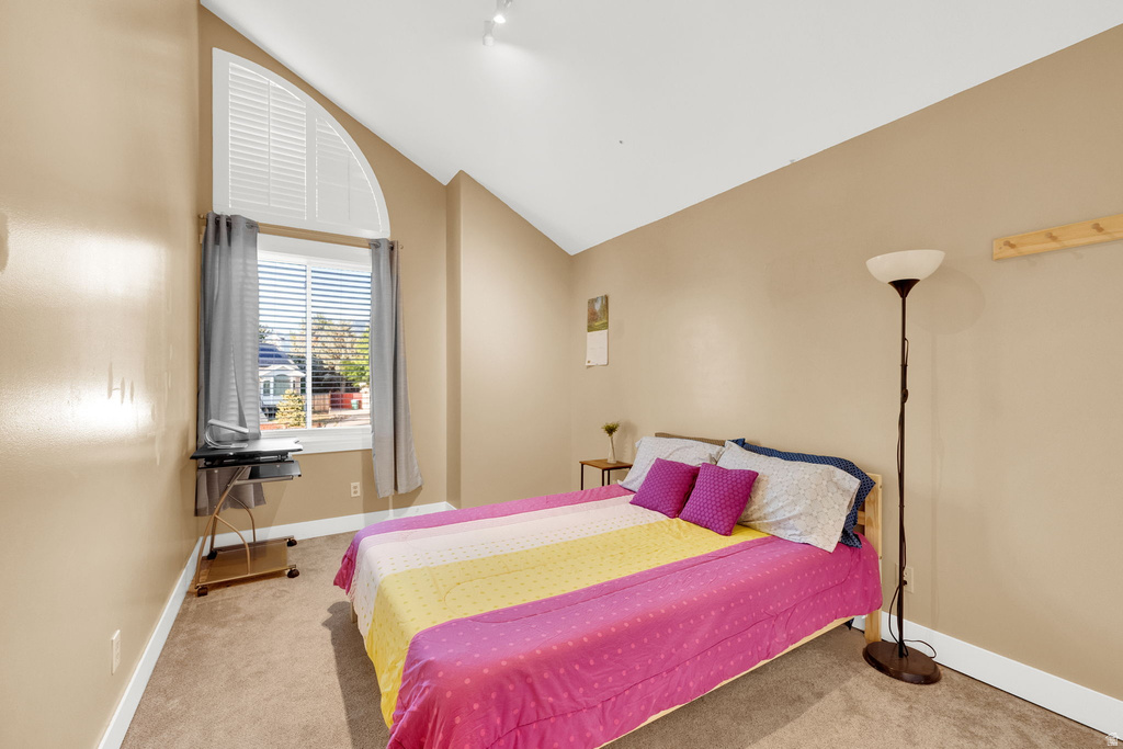 Vaulted ceiling bedroom featuring an arched window with louvered blinds, plush carpet flooring, and neutral wall tones