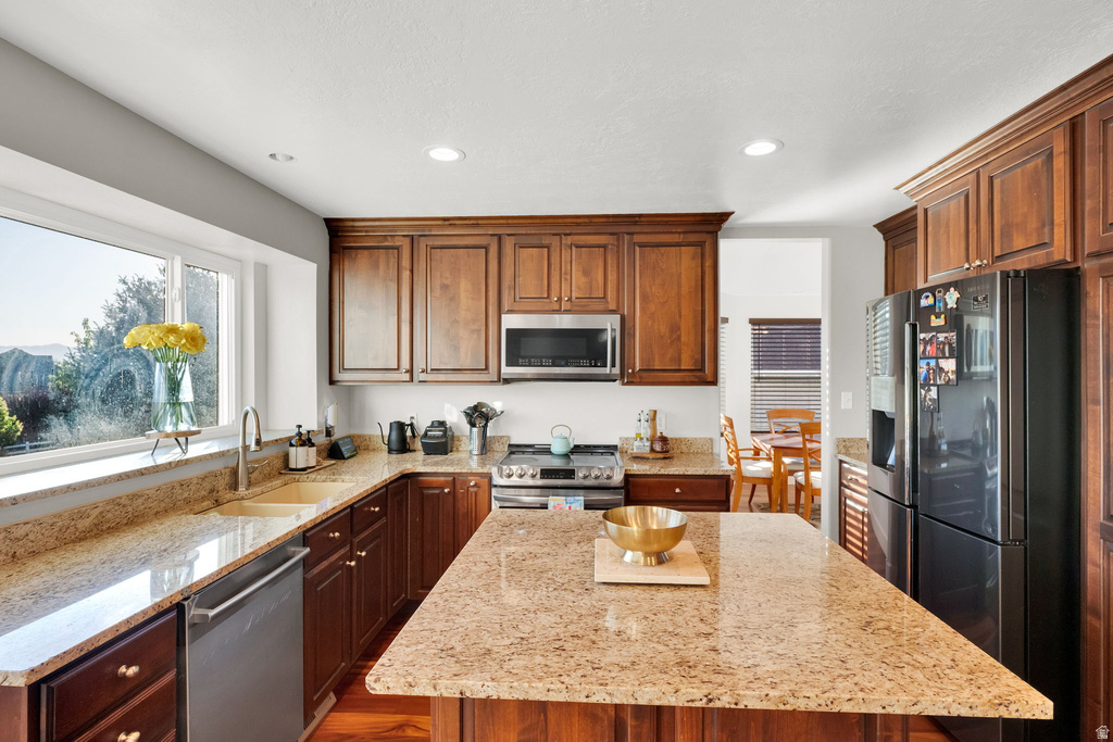U-shaped kitchen featuring wood cabinetry, light-toned granite countertops, stainless steel appliances, and a central island