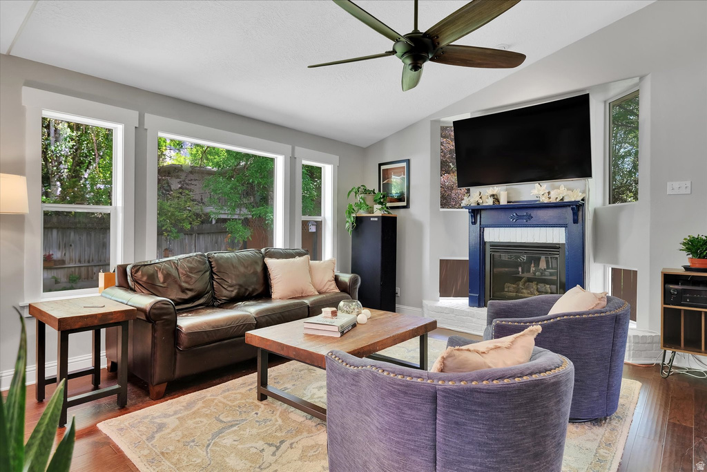 Living area featuring ample natural light, a ceiling fan, rich wood-finish flooring, and a decorative fireplace with a blue mantel and white tile surround